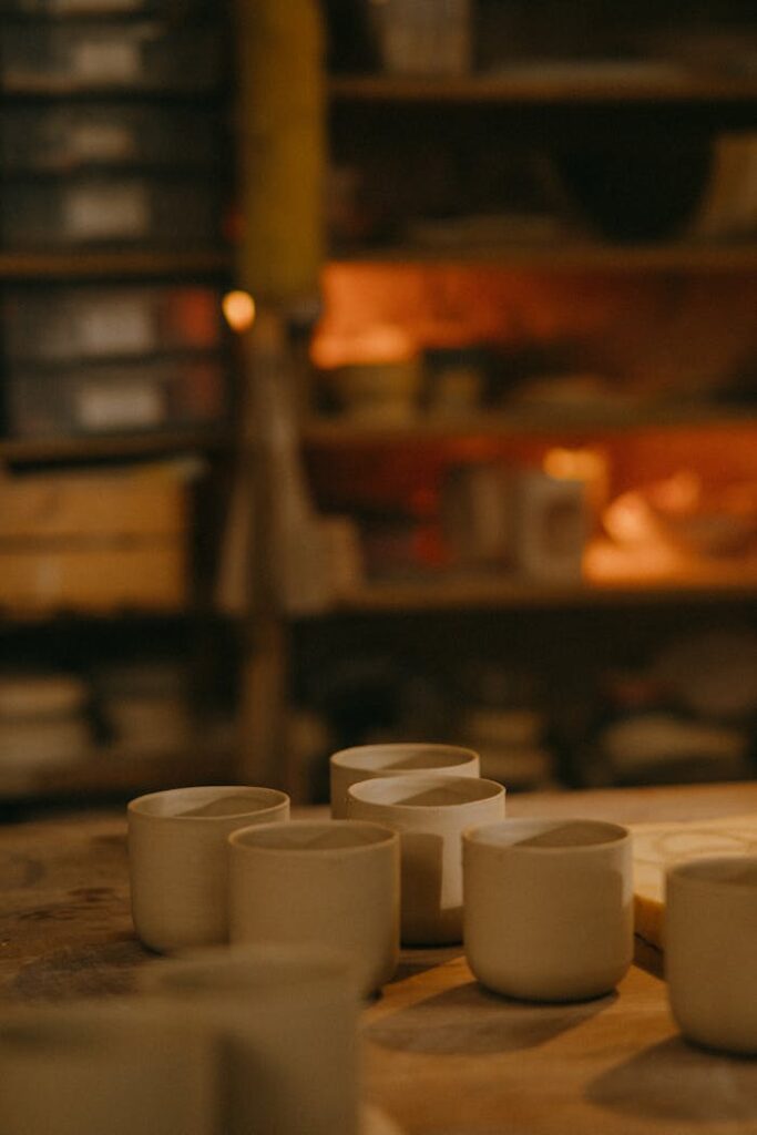 Warmly lit artisan workshop featuring handmade ceramic cups on a rustic table.